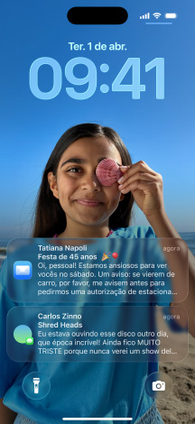 iPhone, cinco modelos, cada um se sobrepondo levemente ao seguinte, os modelos mostram da esquerda para a direita: uma conversa com um plano de fundo no Mensagens; a Tela de Início com ícones de app coloridos; a Tela Bloqueada com uma foto, os números das horas em Liquid Glass e duas notifica??es na parte inferior da tela; os ícones de app transparentes em Liquid Glass; o reprodutor de música em Liquid Glass.