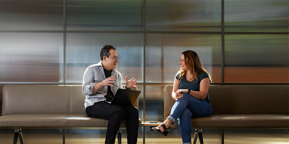 Deux collègues en pleine conversation, assis sur deux bancs dans un espace commun.