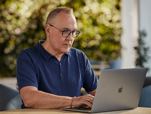 Zaměstnanec z?tymu Software a?slu?by Apple pracuje na MacBooku a?v?pozadí je vidět venkovní zeleň.