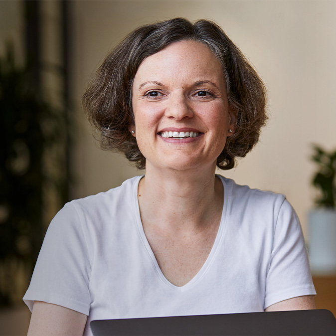 Ruth sedí v?místnosti, usmívá se a?v?pozadí jsou vidět nějaké pokojové rostliny.