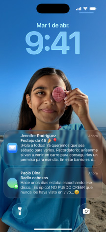 Cinco modelos de iPhone se separan uno detrás del otro, cada modelo se superpone levemente sobre el siguiente, la pantalla del modelo ubicado más a la izquierda muestra una conversación con un fondo en Mensajes, el siguiente muestra la pantalla de inicio con íconos de apps coloridos, el del centro muestra la pantalla bloqueada con una foto y los números de la hora dise?ados con Liquid Glass, así como dos notificaciones en la parte inferior de la pantalla, el siguiente modelo hacia la derecha muestra íconos de apps translúcidos en Liquid Glass y el último a la derecha muestra el reproductor de música hecho con Liquid Glass