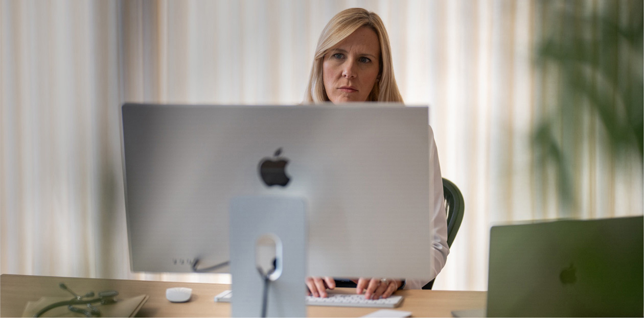 En helsearbeider ser p? en iMac-skjerm ved skrivebordet sitt.