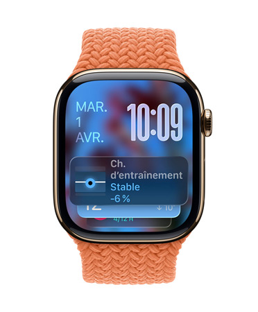 Une Apple Watch or rose avec un Bracelet tressé tangerine, le cadran affiche la date en haut à gauche, l’heure en chiffres superposés en haut à droite, le widget Charge d’entra?nement en bas, le tout en Liquid Glass translucide