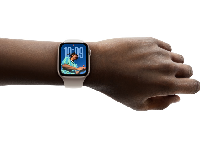 特寫畫面顯示手腕上戴著配上橡膠錶帶的銀色 Apple Watch，展示全新 Liquid Glass 設(shè)計的時鐘 app