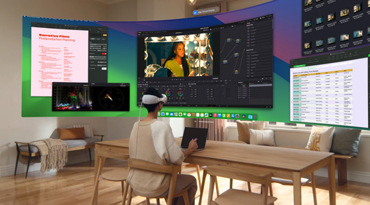 Apple Vision Proを裝著した人が13インチMacBook Proを開いてデスクに座っている。畫面の內(nèi)容が表示されたカーブしたウルトラワイドディスプレイが部屋に投影されている