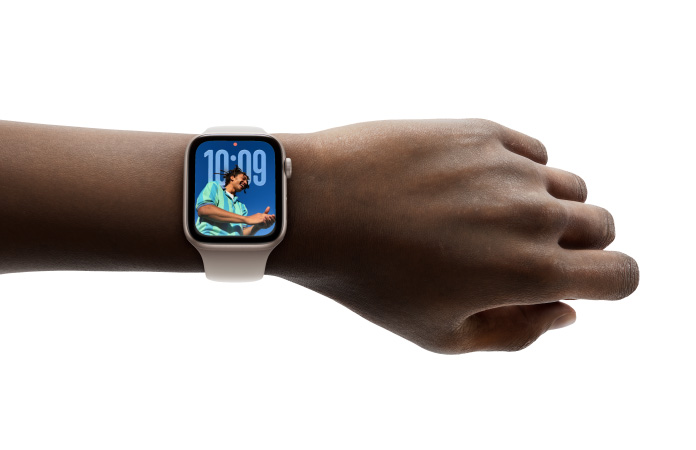 Primer plano de la mu?eca de una persona con un Apple Watch en color plata y correa de goma, cuya pantalla muestra la hora en el nuevo dise?o con Liquid Glass