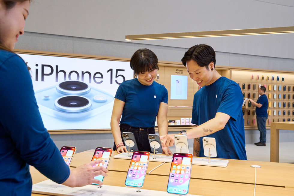 Hình ?nh ??i ng? nhan viên ?ang ng?m nhìn các thi?t b? iPhone 15 trên bàn tr?ng bày trong c?a hàng.