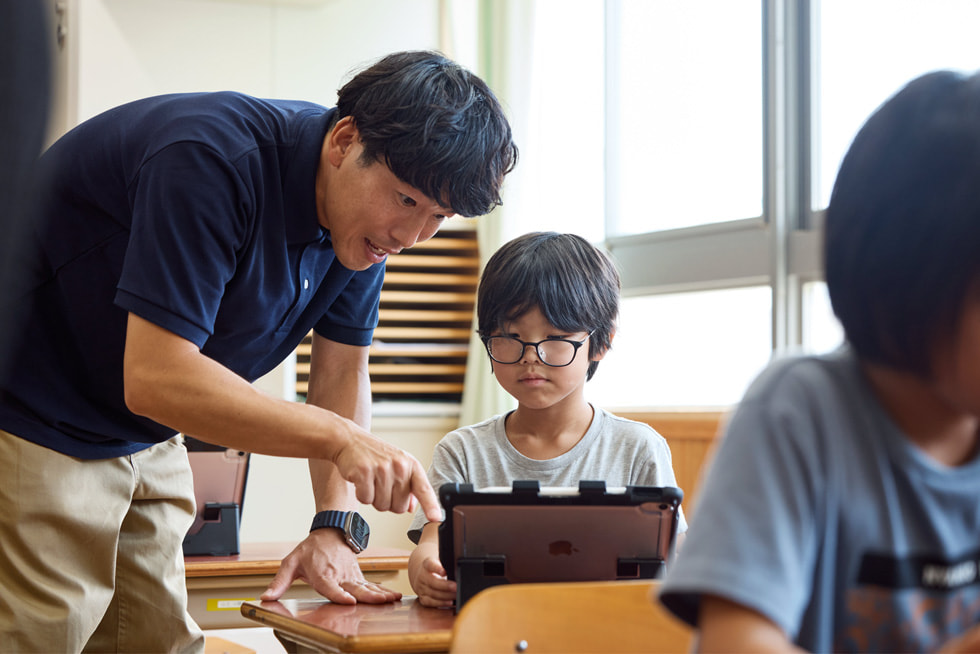 京都市の小學(xué)校の教室で、機(jī)でiPadを使って子どもと一緒に作業(yè)する教師。