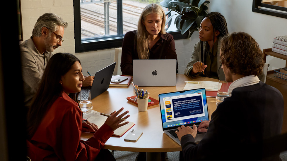 A group works on multiple MacBook Pro devices in a conference room setting.