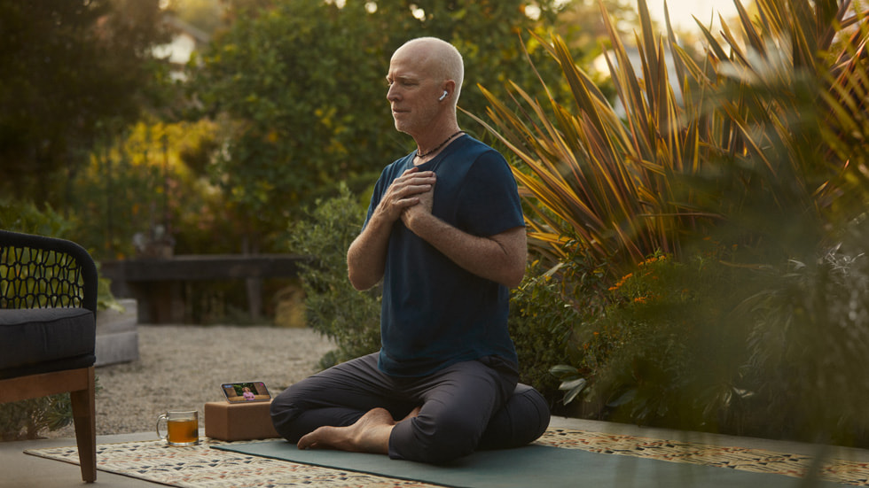 Ng??i ?àn ?ng ?eo AirPods ?ang t?p Yoga trên Fitness+ ngoài tr?i th?ng qua iPhone 14.