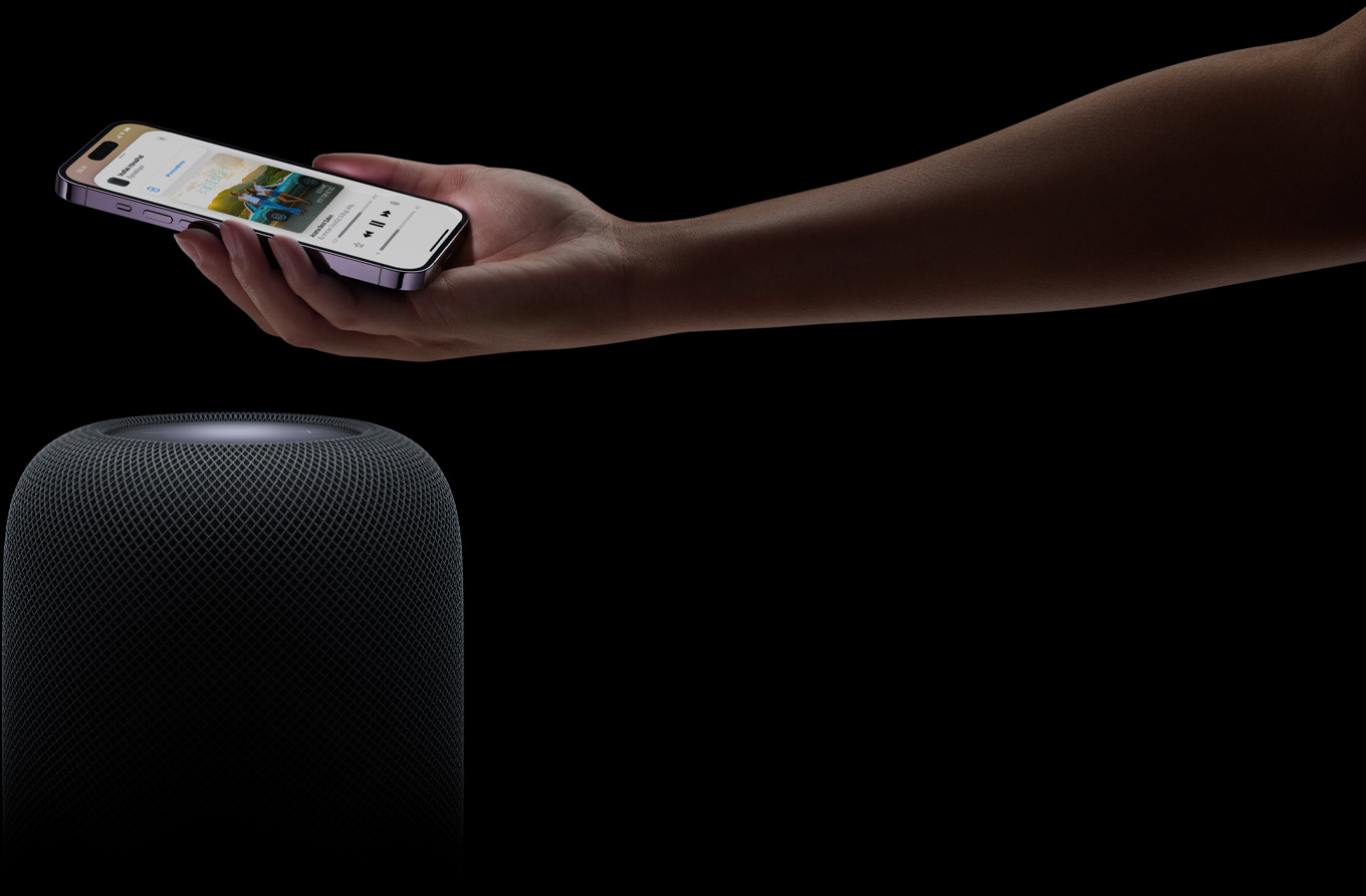 Sayfan?n sa? taraf?ndan gelen bir el, bir HomePod hoparl?rün üstünde bir iPhone’u tutuyor