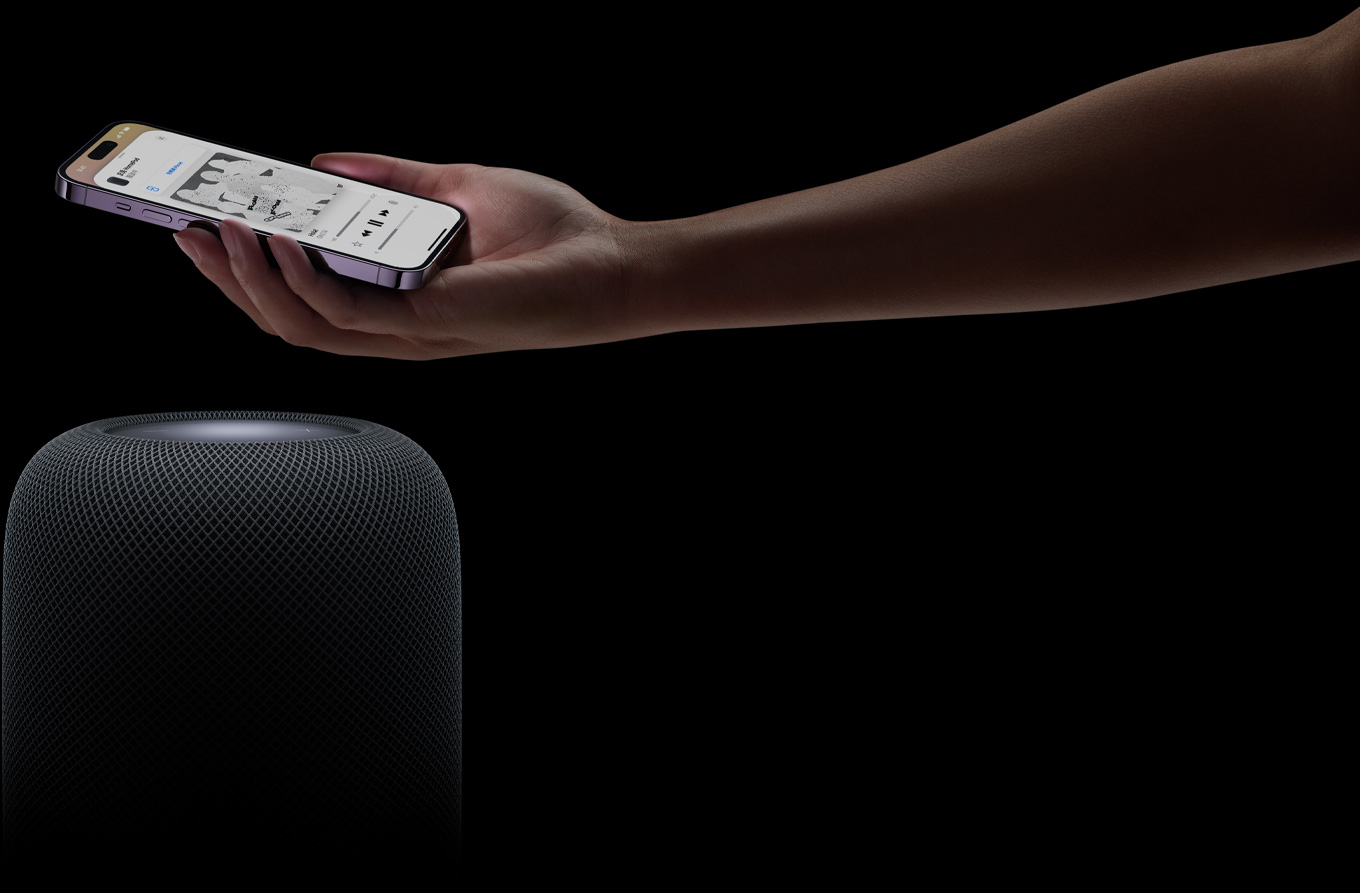 從頁(yè)面右側(cè)伸入的手拿著 iPhone 舉放在 HomePod 揚(yáng)聲器上方