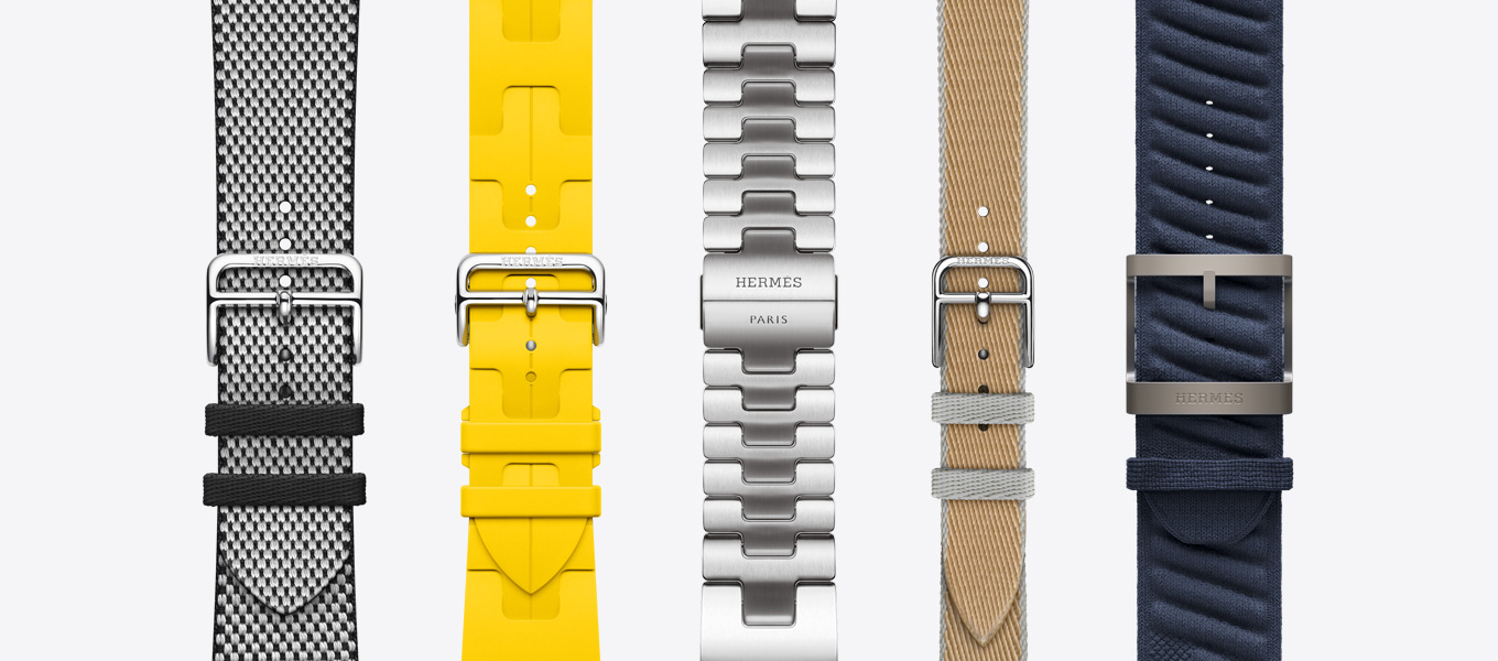 Front view of five Hermès watch straps showing a Noir/écru (black/white) Toile H Single Tour, a Sun (yellow) Kilim Single Tour, a Satiné Grand H, a Kraft/Bleu Glacier (tan/ice blue) Twill Jump Attelage Single Tour and a Bleu Nuit (navy blue) En Mer.