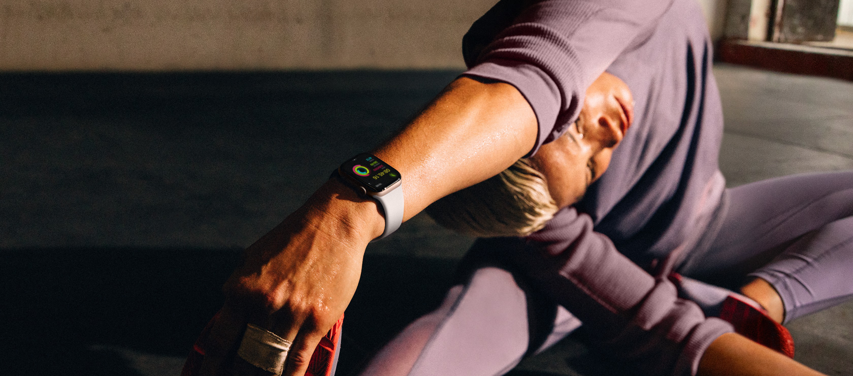 A woman on the floor stretching her arm to her leg while wearing an Apple?Watch Series?10.