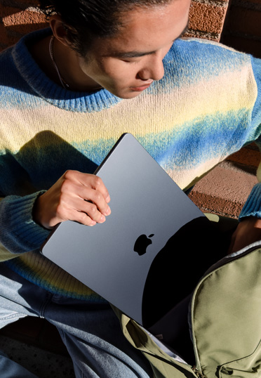 屋外で座っている學生。バックパックから閉じた狀態(tài)のMacBookを取り出している