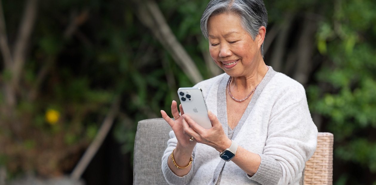 En eldre kvinne ser p? en iPhone mens hun sitter i en stol.