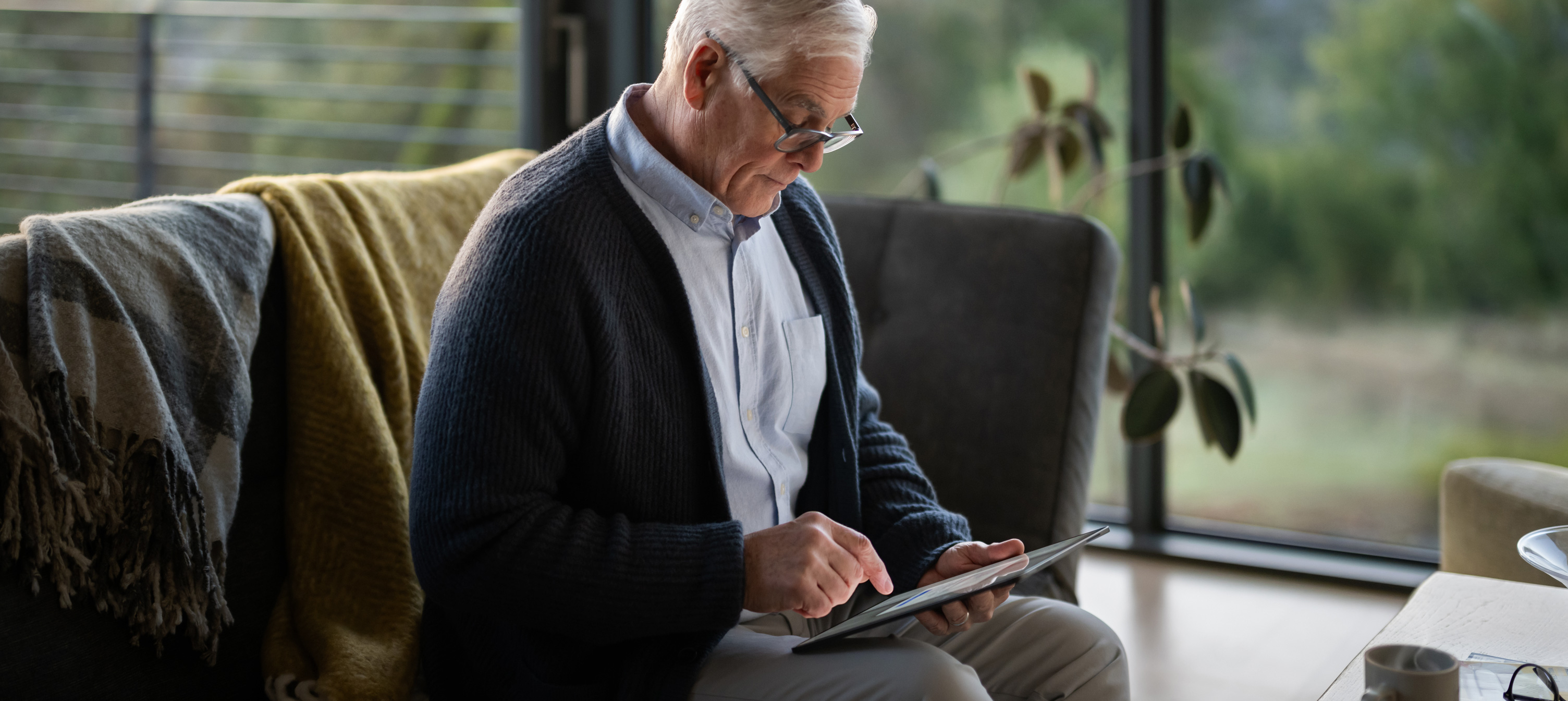 En eldre mann sitter i en sofa og ser p? en iPad.