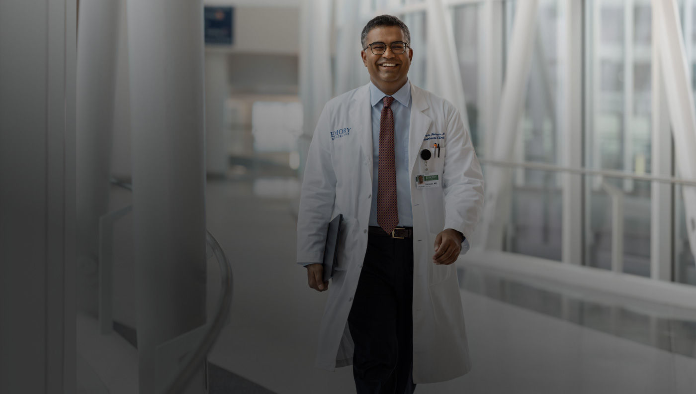 Médico segurando um MacBook embaixo do bra?o direito enquanto caminha.