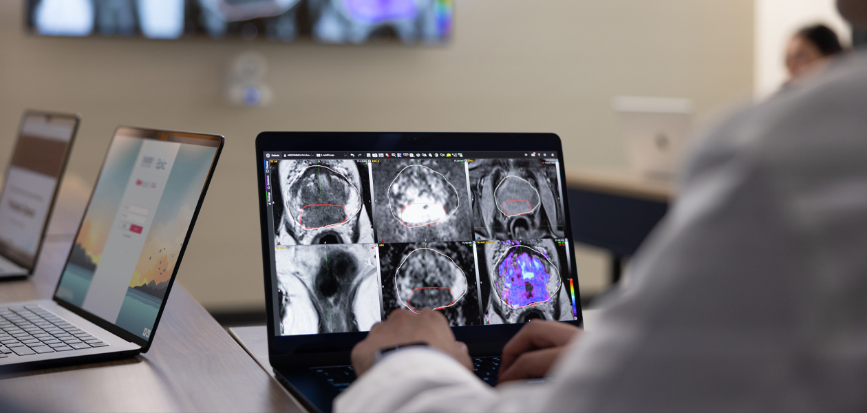 Pessoa revisando exames médicos em um MacBook. Dois outros aparelhos MacBook est?o abertos no fundo.