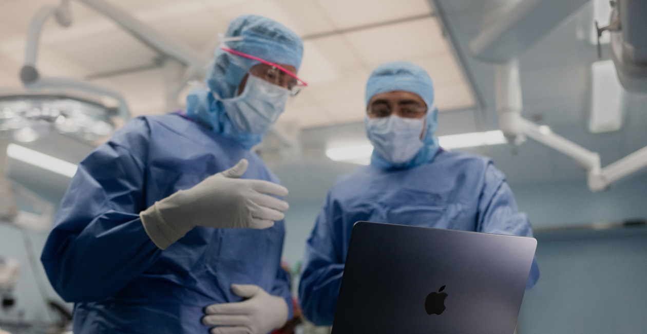 Two surgeons discussing something on the screen of a MacBook Pro in the operating room.