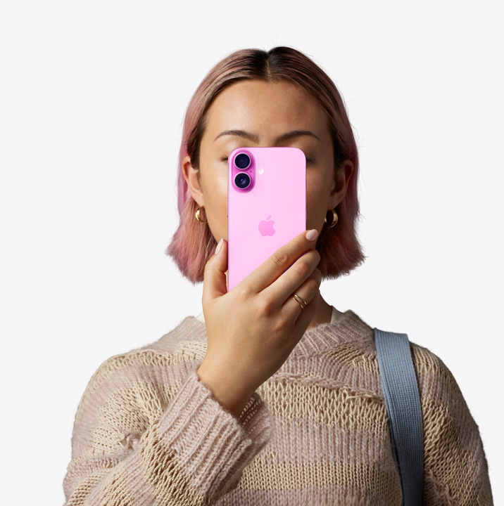 一個人將粉紅色外觀的 iPhone 16 拿到自己面前，展示機(jī)身背面，雙相機(jī)系統(tǒng)位於左上角。