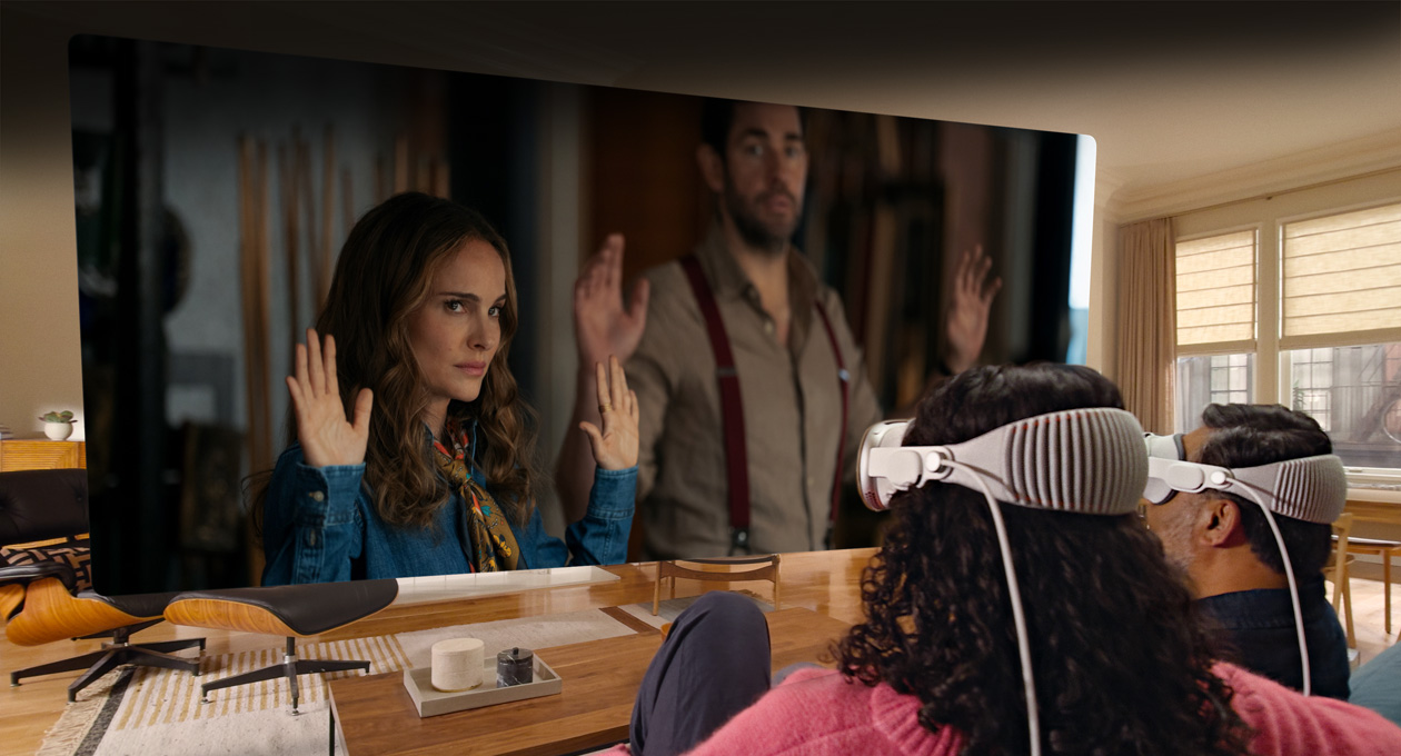 Two people both wearing Apple Vision Pro sit side by side on couch watching: Fountain of Youth movie, displayed on screen stretching across room