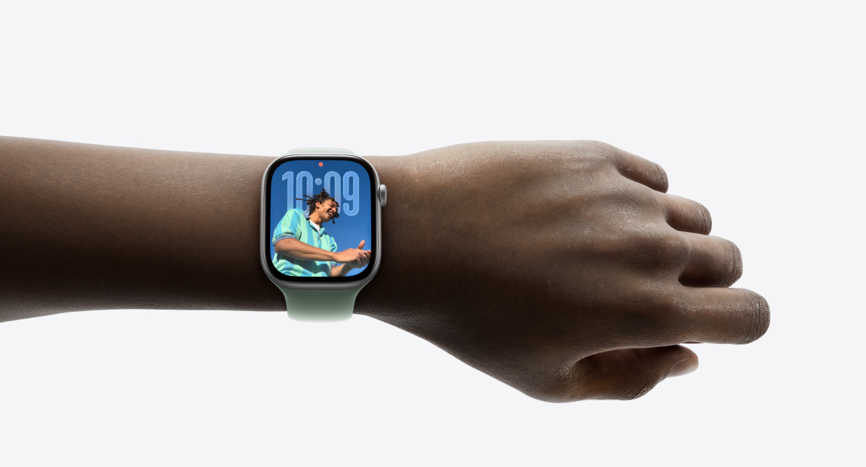 Close-up of Apple Watch in Silver with rubber band on a person’s wrist, showing Time app in new Liquid Glass design
