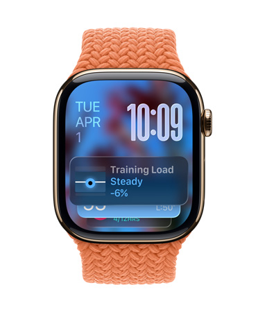 Apple Watch in Gold Titanium with a braided band in Tangerine, face shows date at top left, time with stacked numerals at top right, Training Load widget at bottom, all in translucent Liquid Glass